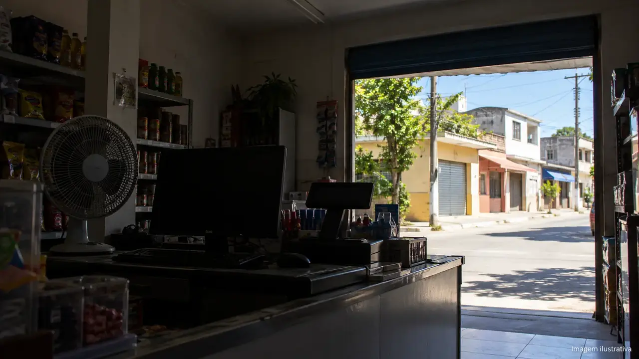 Interior de comércio com luzes apagadas e telas desligadas, enquanto a rua recebe luz do sol.
