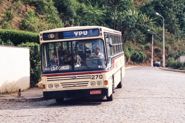 Ônibus 334 com pintura clara e faixas azuis e vermelhas, estacionado em piso de paralelepípedos.
