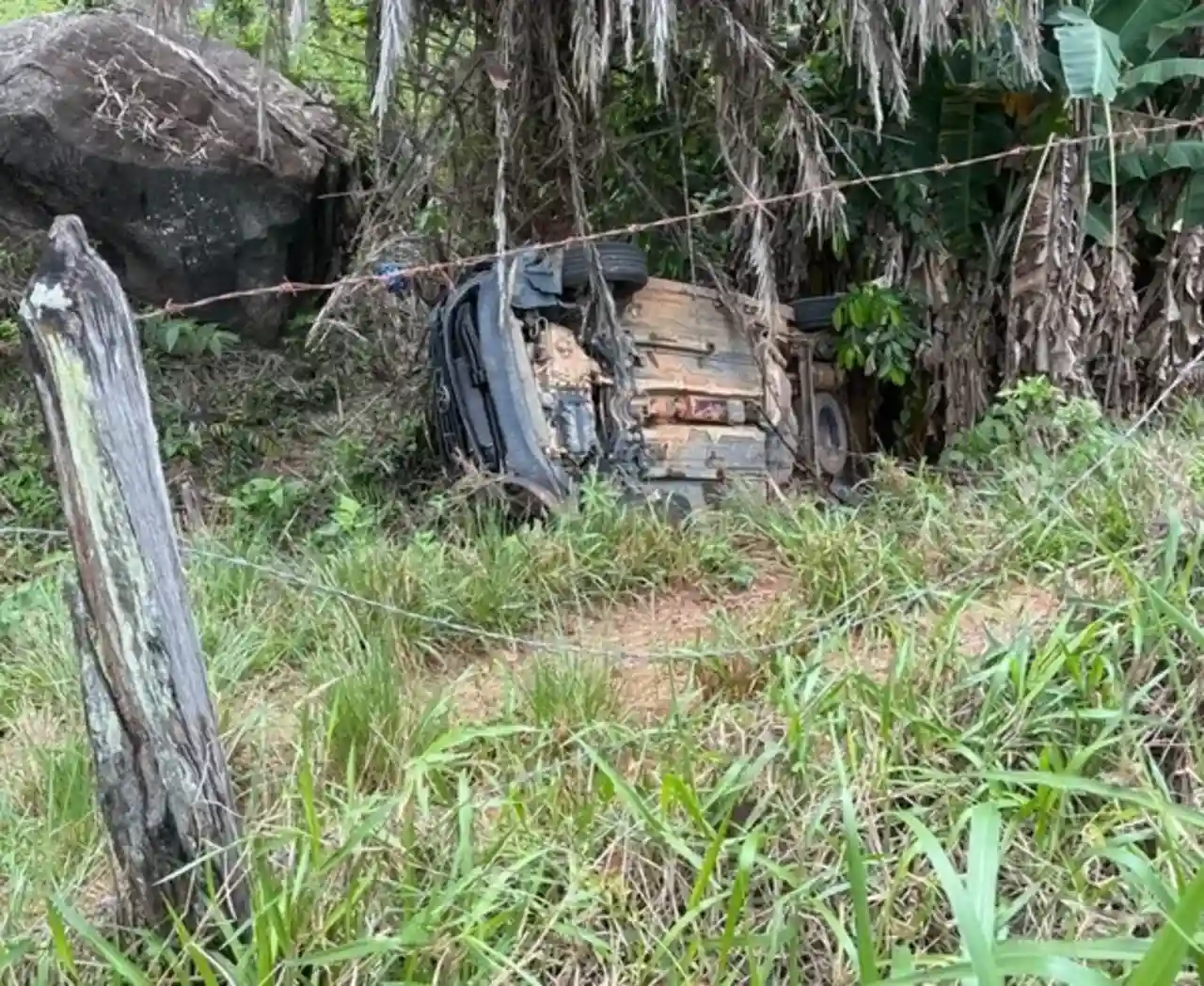 Carro capotado entre árvores e vegetação em Euclidelândia, Cantagalo.