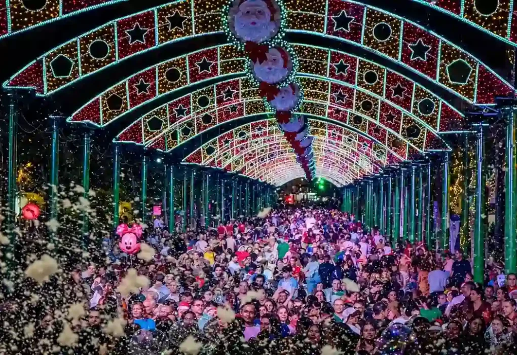 Público sob arcos de iluminação natalina com estrelas e figuras de Papai Noel em Nova Friburgo.