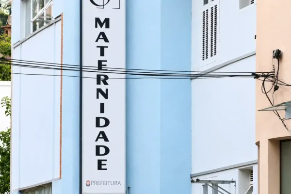 Fachada azul-clara da maternidade de Nova Friburgo, com identificação vertical do hospital.