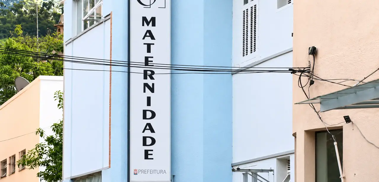 Fachada azul-clara da maternidade de Nova Friburgo, com identificação vertical do hospital.