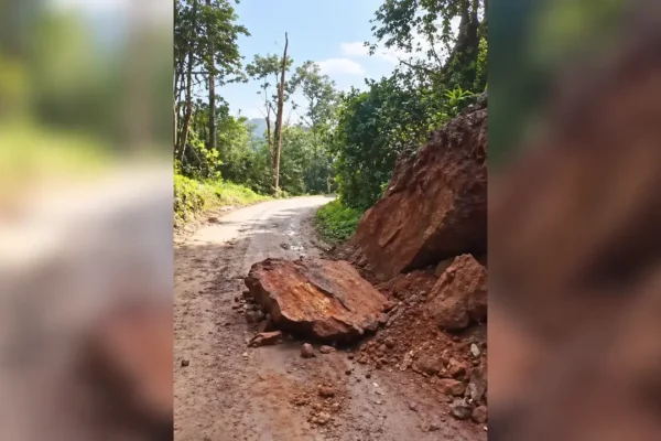 Pedra de grande porte e terra sobre parte de uma estrada rural, junto a uma encosta cercada por vegetação.