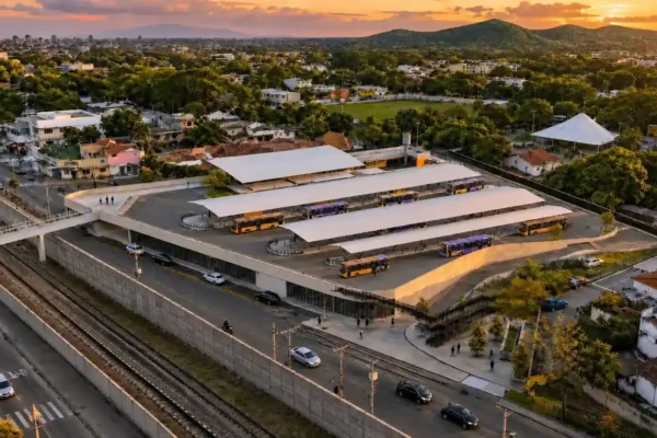 Vista aérea de terminal de ônibus com plataformas cobertas, ao lado de uma linha férrea, ao pôr do sol.