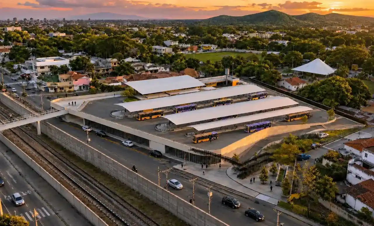 Vista aérea de terminal de ônibus com plataformas cobertas, ao lado de uma linha férrea, ao pôr do sol.