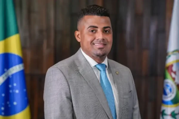 Ex-deputado estadual TH Joias de terno cinza e gravata azul, entre bandeiras.