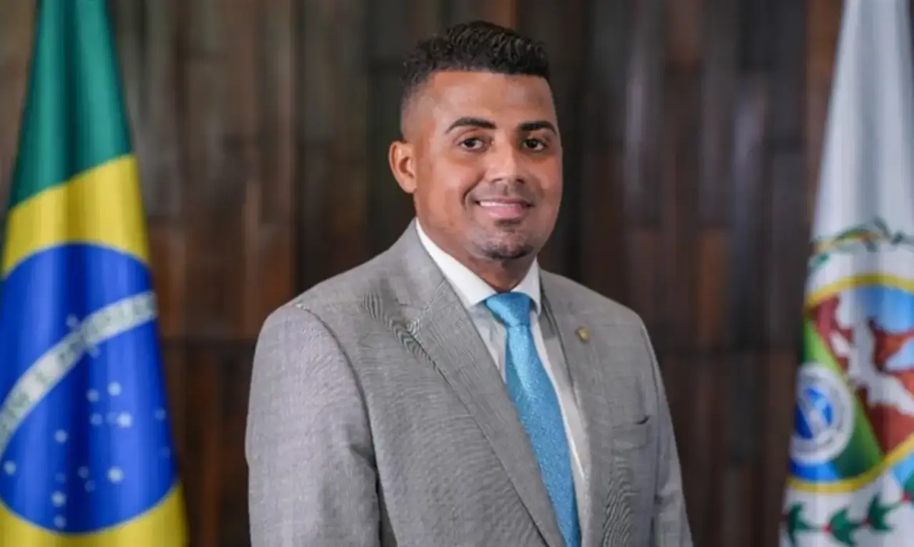 Ex-deputado estadual TH Joias de terno cinza e gravata azul, entre bandeiras.